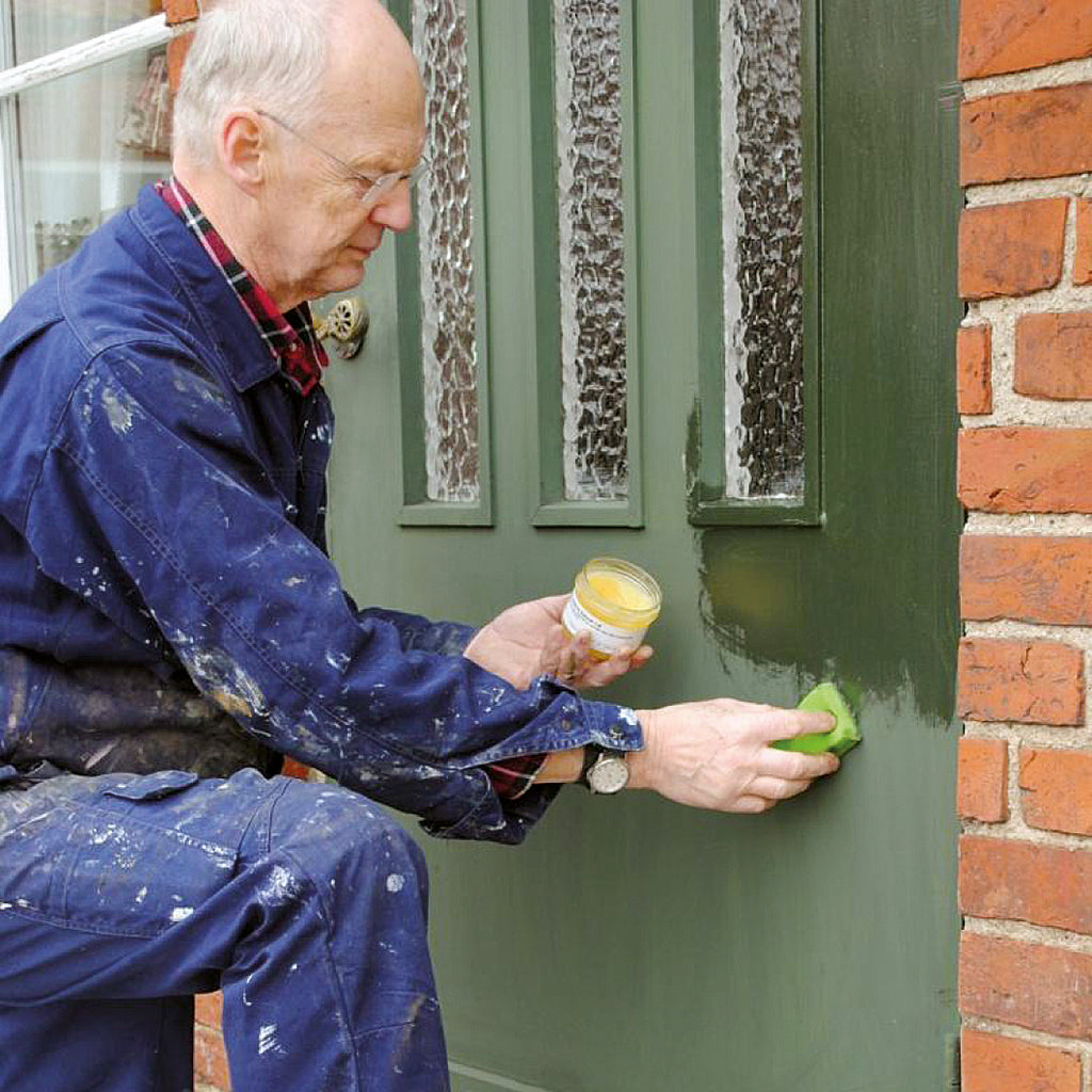 Hans Allbäck applying Clear Linseed Oil Wax to revive the faded, green linseed oil paint on an exterior door.