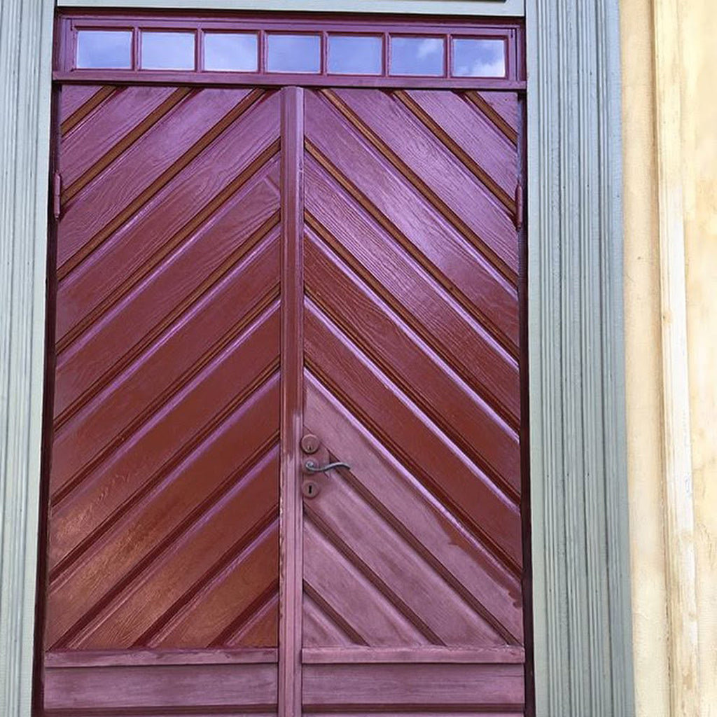 Exterior wooden door with a chevron pattern and glass transom panels, showing faded, chalky red linseed oil paint, almost fully revived to its original colour and sheen with Allbäck Linseed Oil Wax.