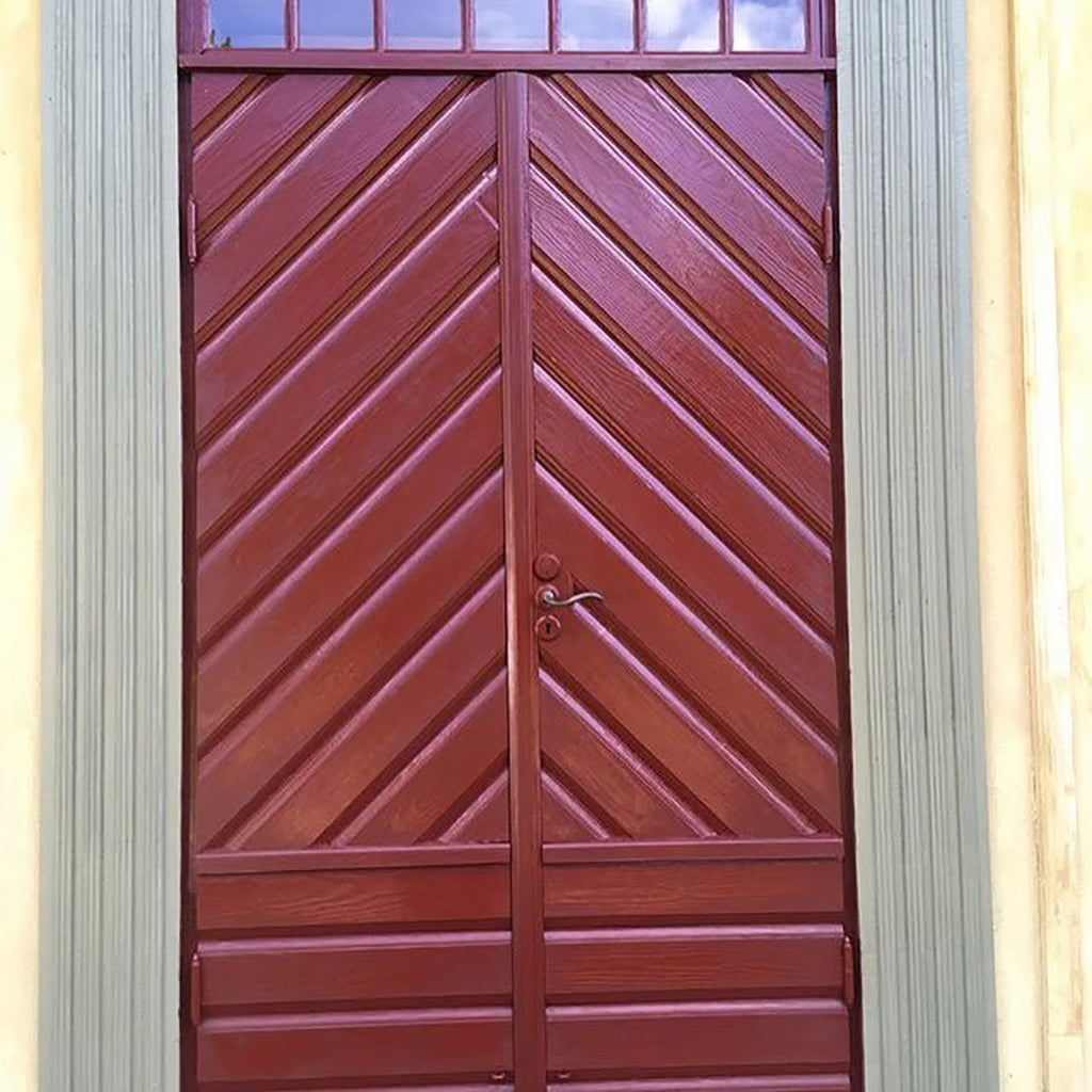 Exterior wooden door with a chevron pattern and glass transom panels, showing red linseed oil paint that has been fully revived to its original colour and sheen with Allbäck Linseed Oil Wax.