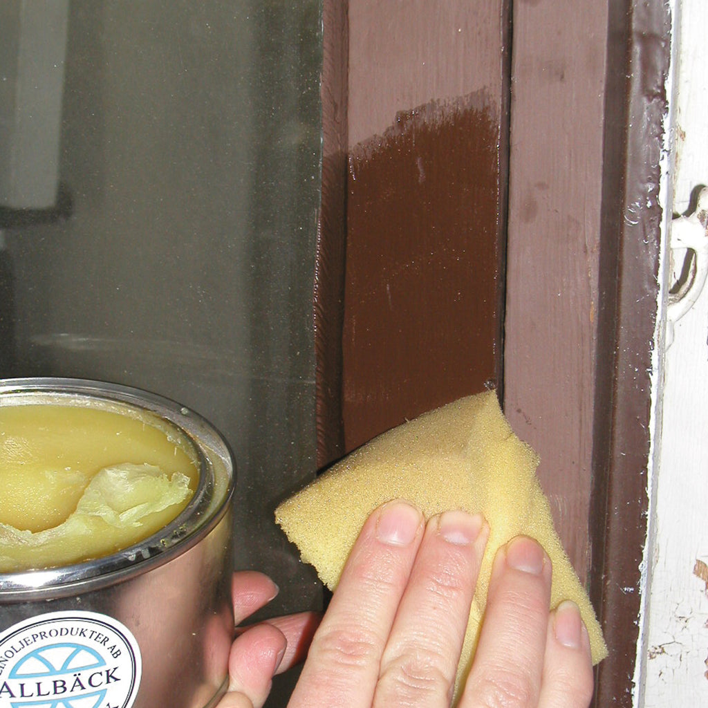 Hand with yellow sponge applying clear Linseed Oil Wax to revive the faded, brown Linseed Oil Paint around a window frame.