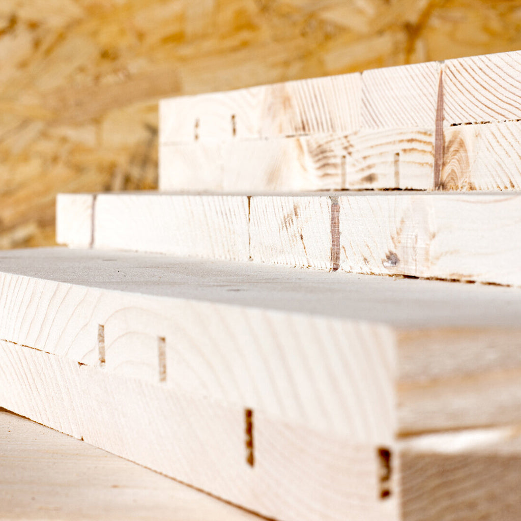 A stack of structural wood panelling waiting for installation, using the LIGNOLOC® Wooden Nail System.