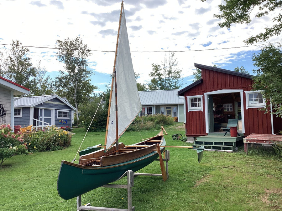 Wooden canoe with a sail in front of the red boat shed