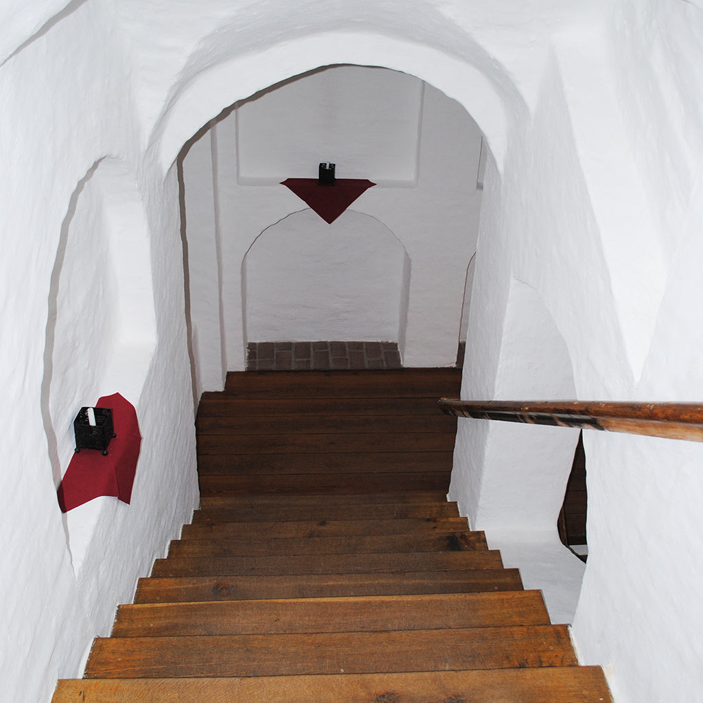 Wooden staircase in an old Swedish citadel building, freshly treated with Allbäck's Natural (Clear) Linseed Oil Wax. The staircase is leading down to an arched hallway with white, plaster walls.