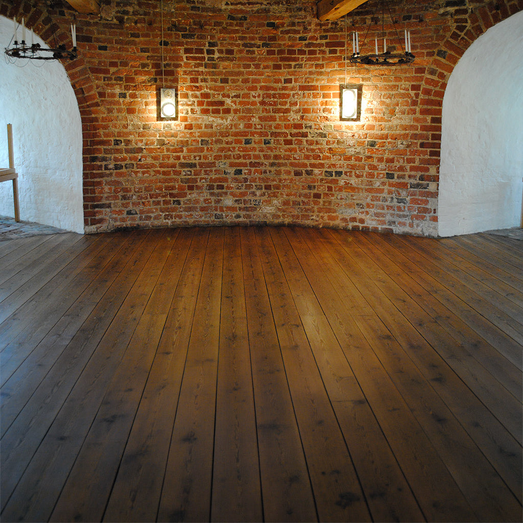 Old pine floor, freshly restored with Natural (Clear) Allbäck Linseed Oil Wax, in a large room in an old citadel in Sweden, with white plastered walls and a high ceiling with exposed wood beams.