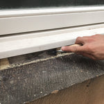 Smoothing Sand Mastic between a window frame and stone sill with a stainless steel trowel.