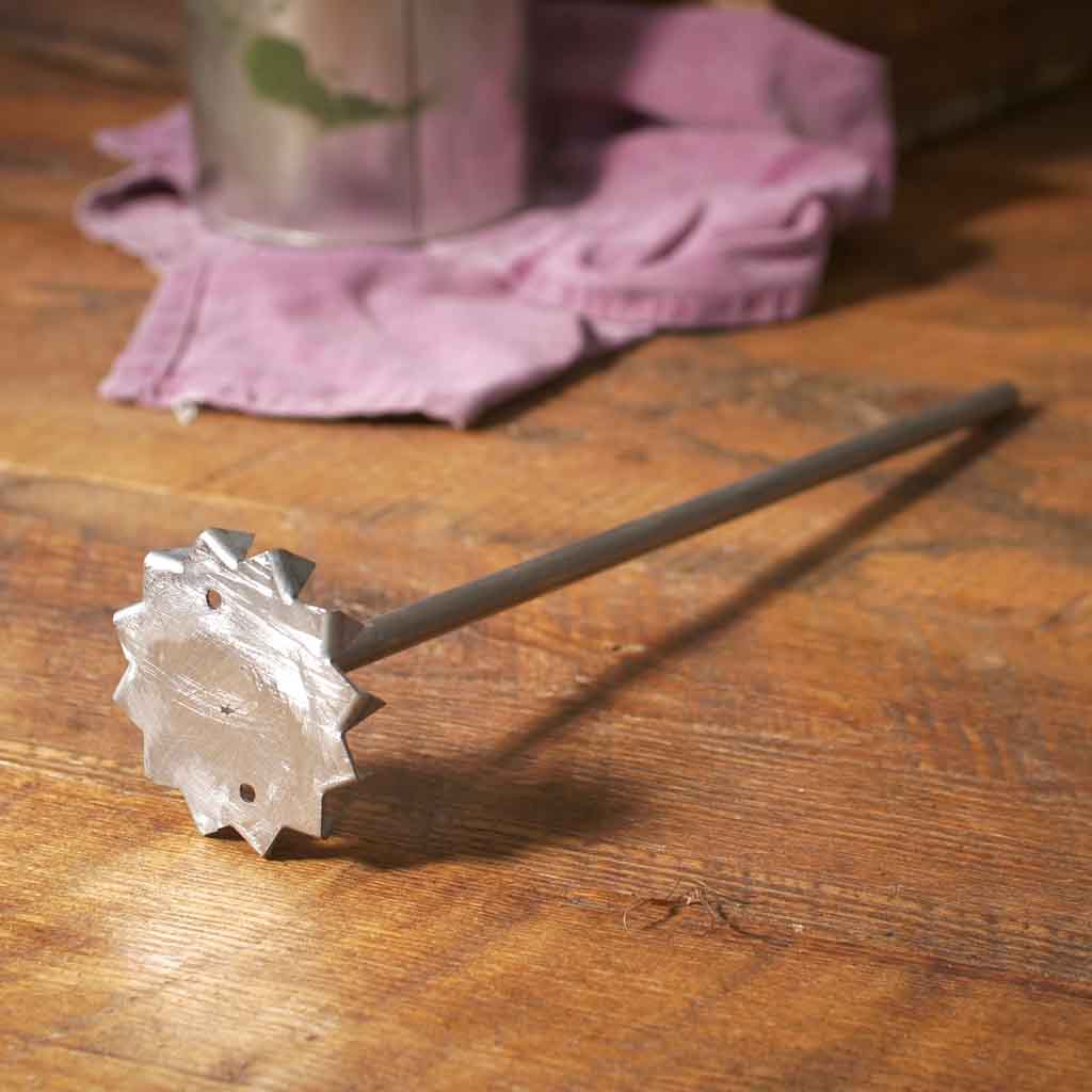 Metal paint mixer on a wood surface with a pain can and pink towel in the background.