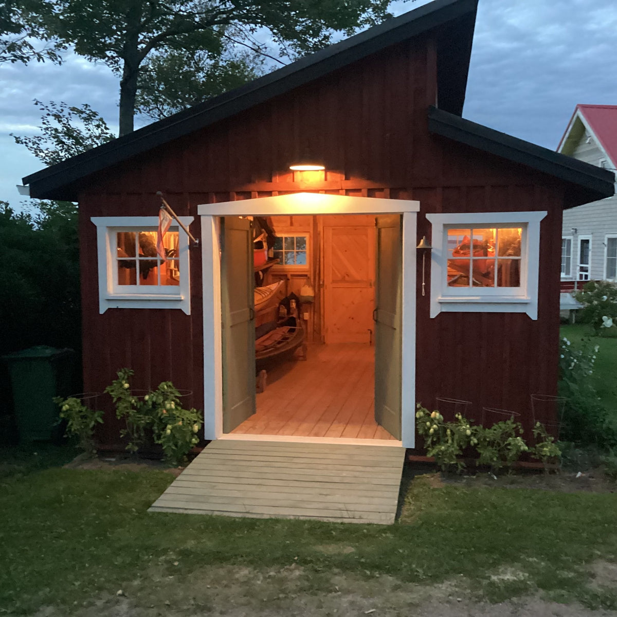 The red boat shed at dusk with the doors open and the lights on