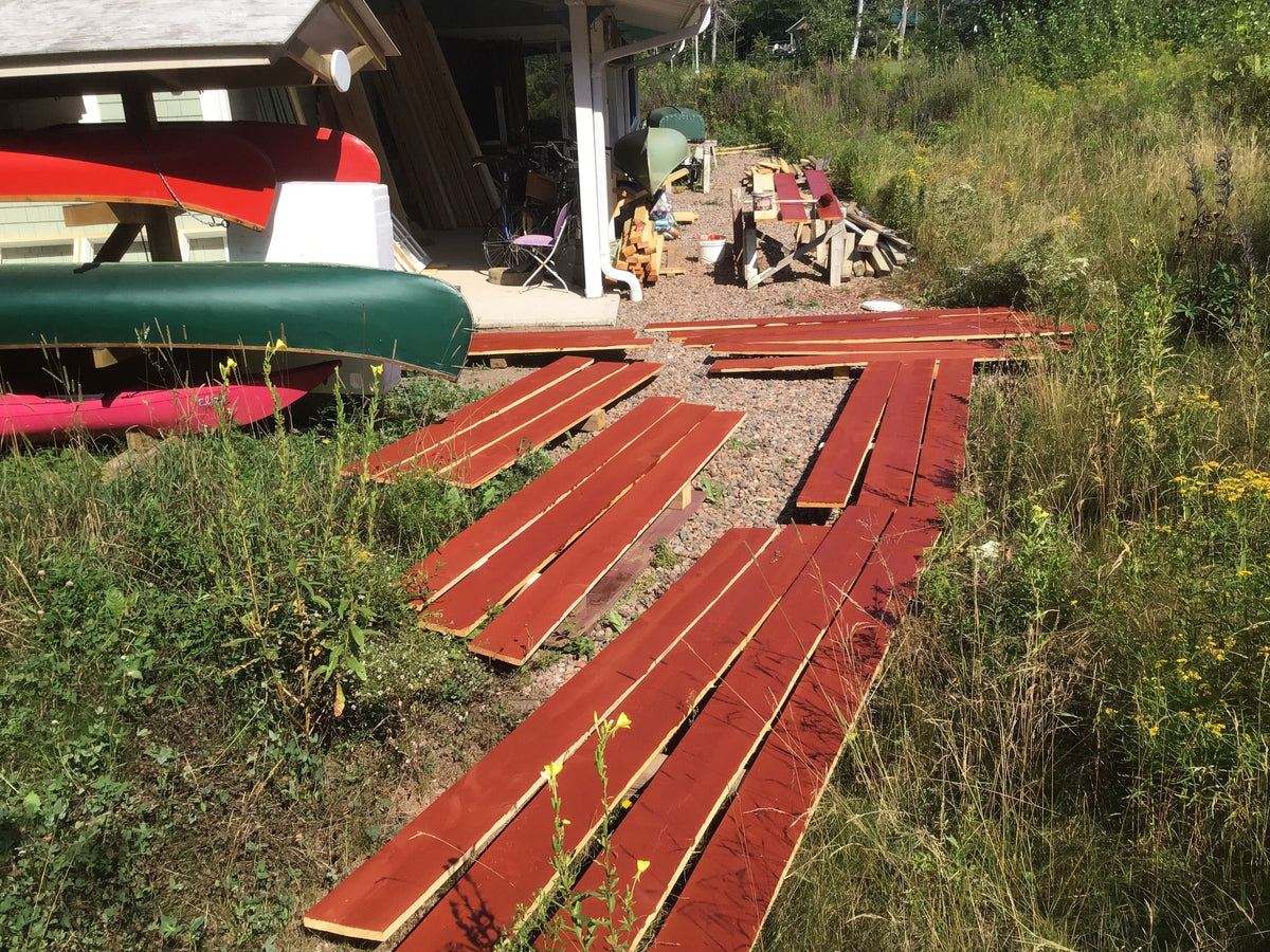 Spruce planks freshly coated in red pine tar laid out on the grass