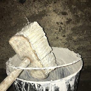 Lime wash brush resting on the mixing bucket, waiting to apply hot mixed lime wash to a cellar wall.